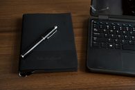 A minimalist office setup with a notebook, pen, and laptop on a wooden desk.